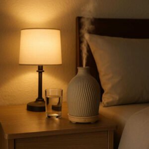 Diffuser til æteriske olier i Høj Kvalitet - Stilfuldt Keramisk Design med Ribbet Tekstur til Bedre Hjemmemiljø: A different realistic bedroom setting where the diffuser is securely positioned on a bedside table, being used to create a calming ambiance next to a softly glowing lamp and a glass of water, with proper physics and subtle shadows integrating the product naturally into the cozy nighttime environment.