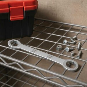 Dobbeltstørrelse Skruenøgle – Professionel og Alsidig Værktøjsløsning med Høj Kvalitet: A different realistic home improvement setting where the Dobbeltstørrelse Skruenøgle is securely positioned on a metal shelf, being naturally placed next to a toolbox and various screws and bolts, indicating readiness for use in a DIY project.