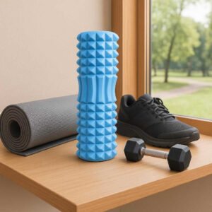 Massagerulle med Dybdegående Struktur i Blå, Lilla, Lyserød, Sort – Professionel Restitution & Komfort. The blue massage roller rests on a wooden shelf beside gym gear, with a window overlooking a scenic park view in the background, evoking a sense of relaxation and wellness.