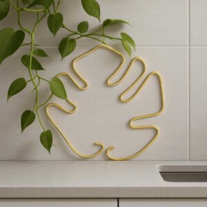 Planteholdere i Messing til Væg - Eksklusiv Dekoration til Hjemmet i Skandinavisk Stil. A close-up of the stylish brass plant holder mounted in a modern kitchen, with trailing green vines adding a fresh touch above a sleek countertop.